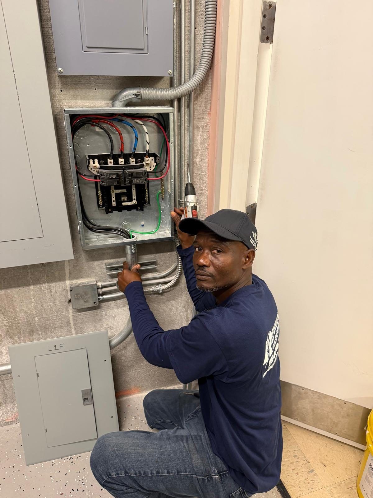 A Reference Electric technician in a branded cap working at an electrical panel