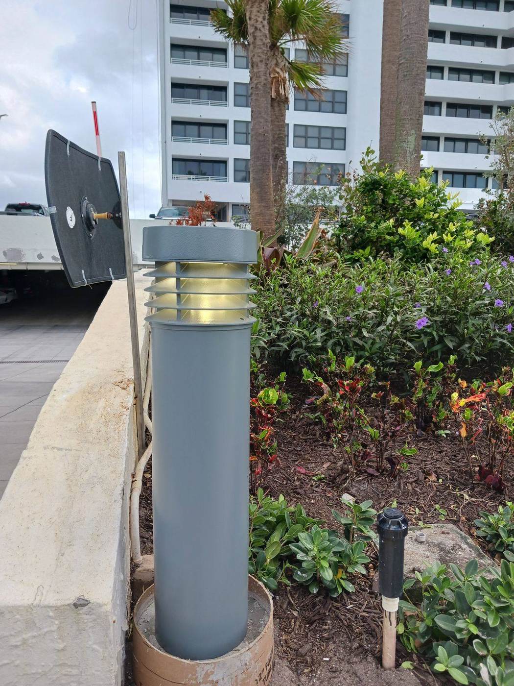 Illuminated bollard path light installed in a landscaped bed beside a walkway