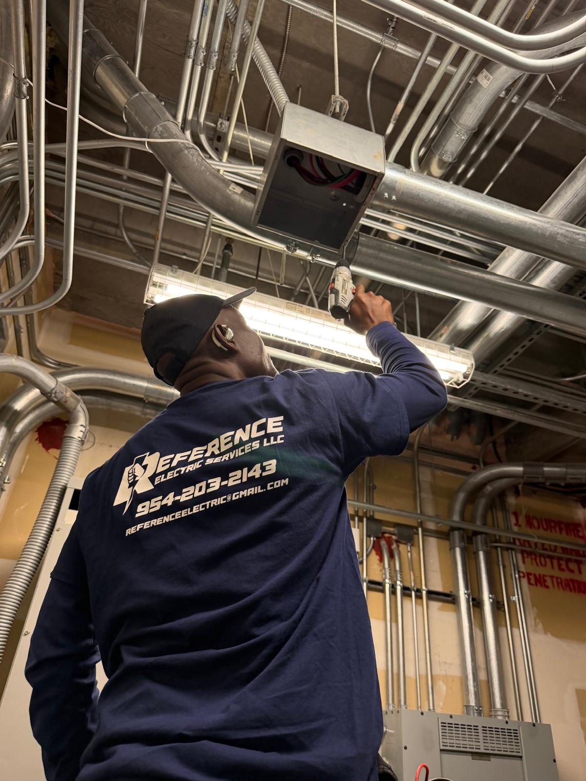 A Reference Electric technician in a branded shirt working overhead on a junction box