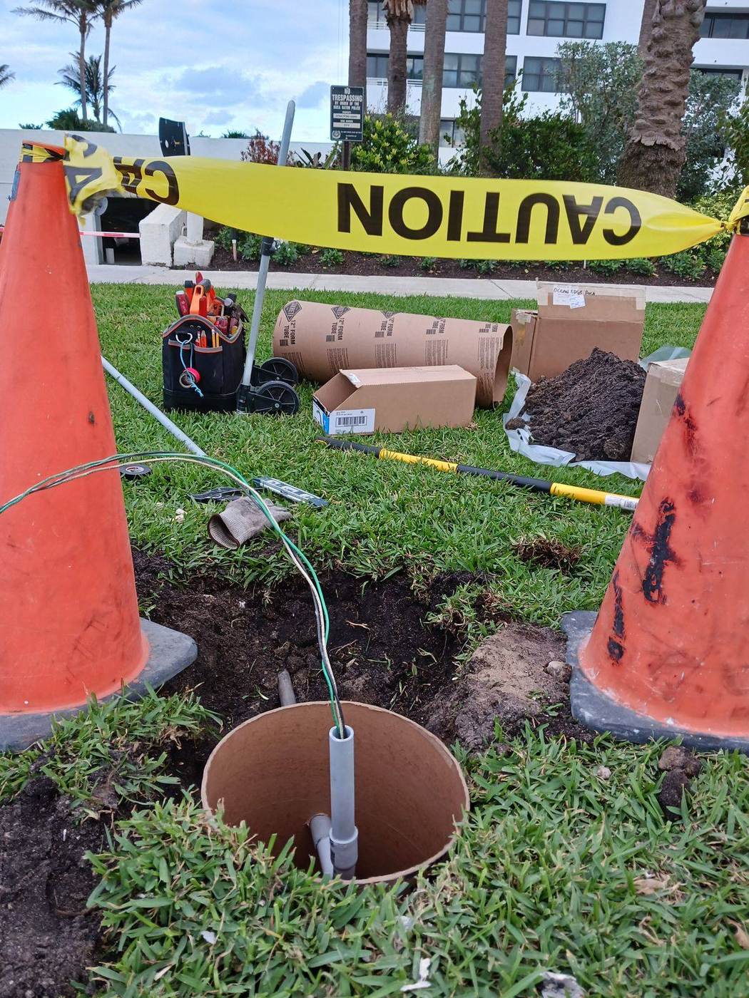 Outdoor lighting installation in progress with concrete form tubes and the work area coned and taped off
