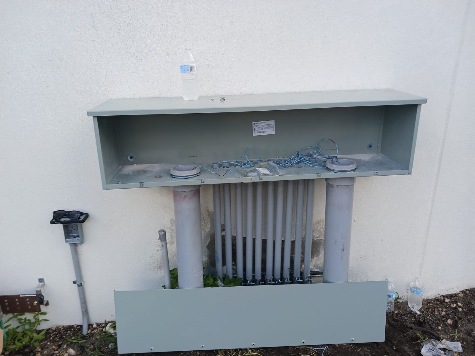Large wireway mounted on an exterior wall with multiple conduit runs below